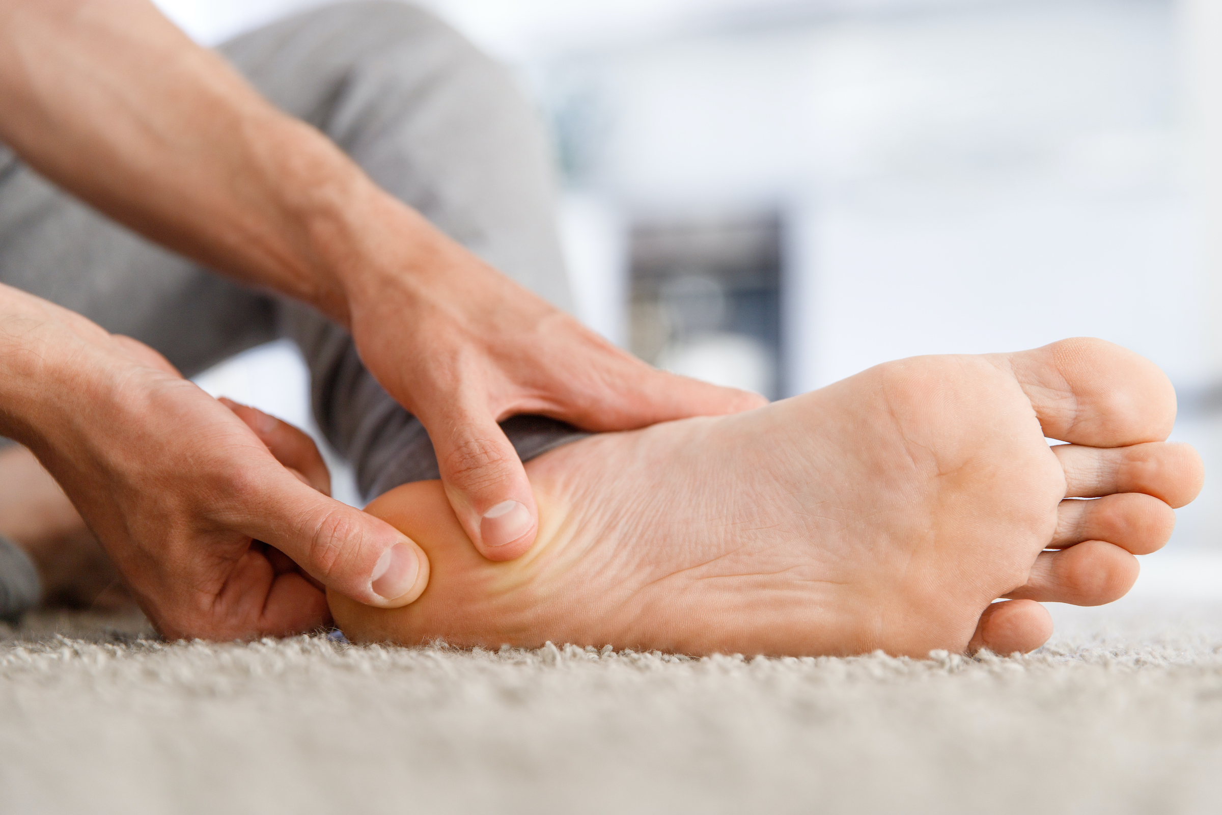 Man hands giving foot massage to yourself after a long walk, suffering from pain in heel spur, close up, indoors. Flat feet, leg fatigue, plantar fasciitis,  (Man hands giving foot massage to yourself after a long walk, suffering from pain in heel spu